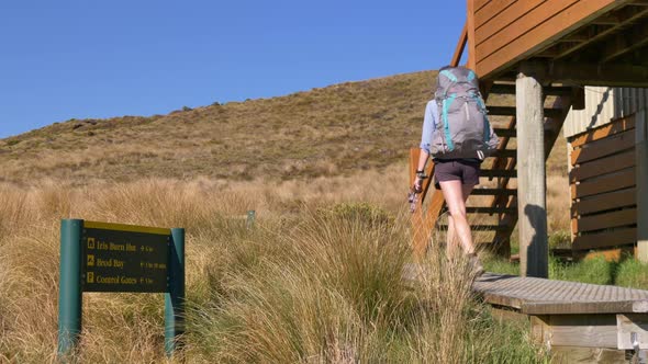 Static, hiker leaves Luxmore Hut past sign, Kepler Track New Zealand alt
