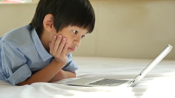 Cute Asian Boy Lying In Bed And Using Laptop On White Bed alt
