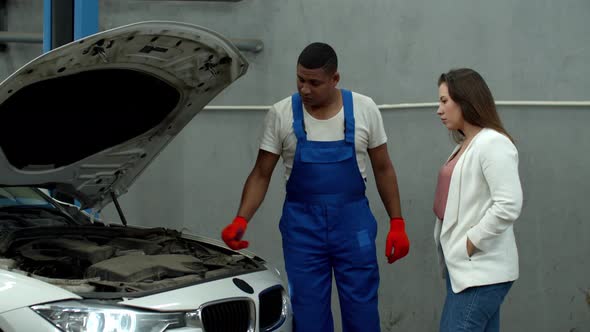 Mechanic Opens the Hood of a Car and Shows the Engine To Woman alt