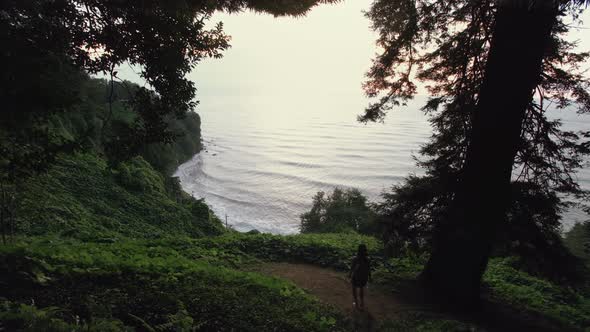 Girl Traveler Goes Down To Cliff Hill in Mountain Forest, Sea Bay and Waves. Tropical Plants, Trees alt