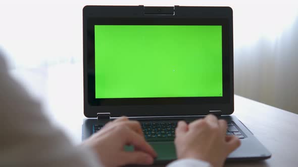 A nurse in a bathrobe is typing on a laptop with a green screen on the table alt