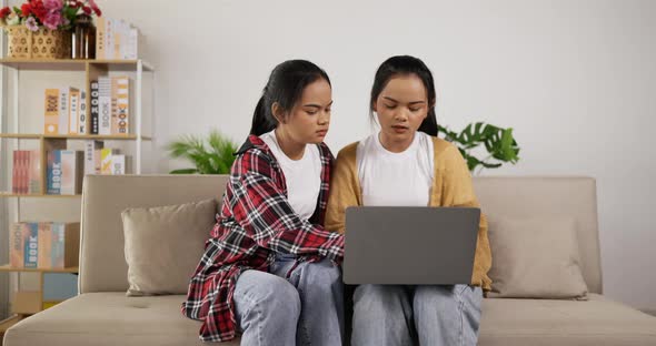 Twin girls planning for work to laptop while sitting on couch alt