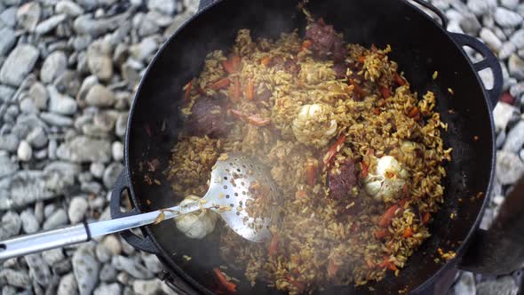 Cauldron with Uzbek Pilaf and Slotted Spoon on the Stove alt