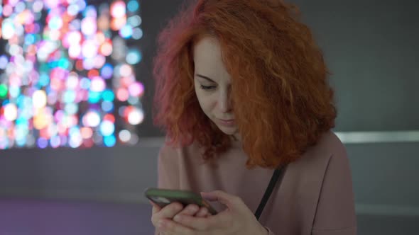 A girl with red hair looks at her smartphone while doing something alt