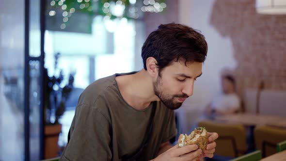 Unshaven c Man Eats Meat Burger with Pleasure Bites Burger with His Mouth alt
