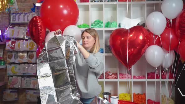 a Woman Inflates a Balloon in the Shape of a Large Silver Numeral for a Birthday alt