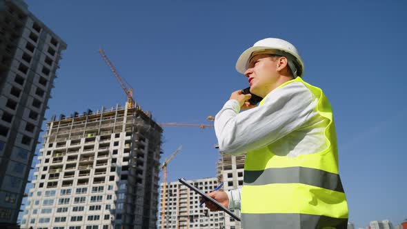 Engineer Talking on Phone and Making Notes at Construction Site alt