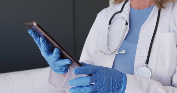 Midsection of caucasian female doctor wearing surgical gloves using tablet computer alt