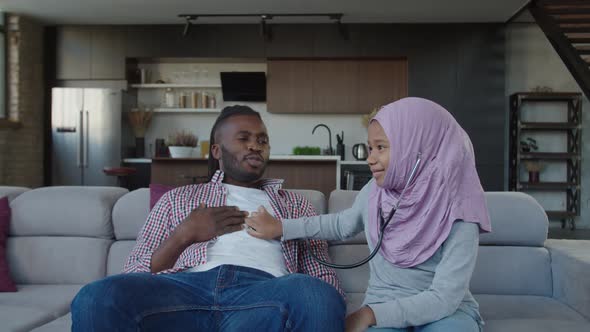 Joyful African Father and Cute Multiethnic Daughter in Hijab Playing Doctor with Stethoscope Indoor alt