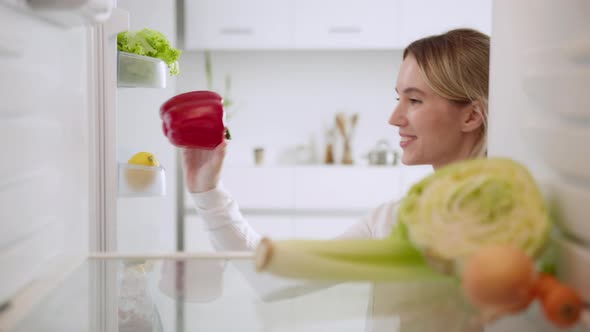 Woman holding grocery bag and unpacking fresh vegetable and fruit into refrigerated