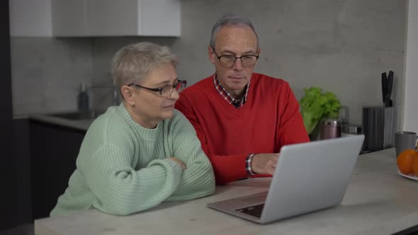 Sad Pensioners Looking at Laptop Discussing Utility Bills Financial Problem or Confusing News alt