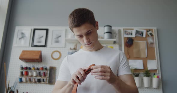 Young Leather Worker with Vitiligo Examining Leather Strip for Making a Belt