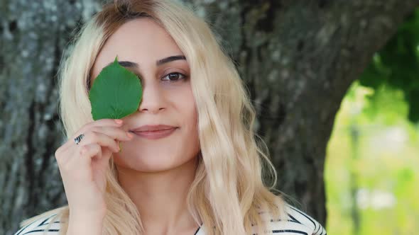 Spring Mood  Blond Caucasian Girl Holding a Small Green Leaf Close to the Eye alt