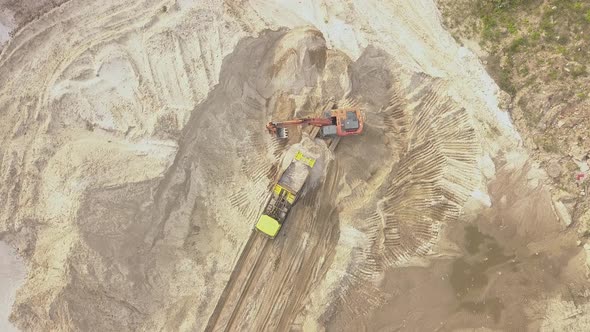Working Machines Pour Sand Into a Loading Excavator in a Quarry There is a Lot of Sand Around alt