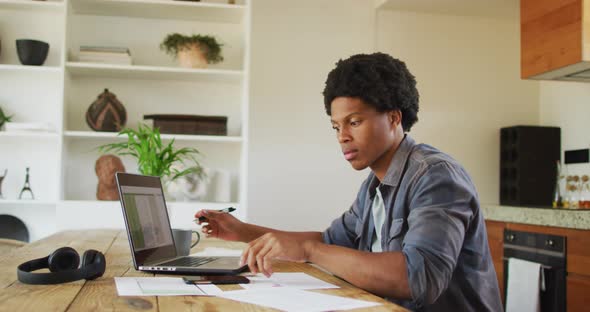African american man working from home and using laptop and smartphone alt