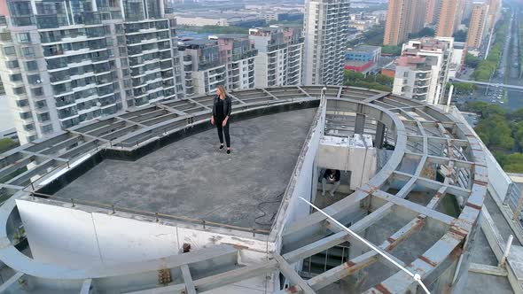 Aerial Orbital Shot of Beautiful Blond European Girl Standing on the Roof Top of Modern Apartments alt