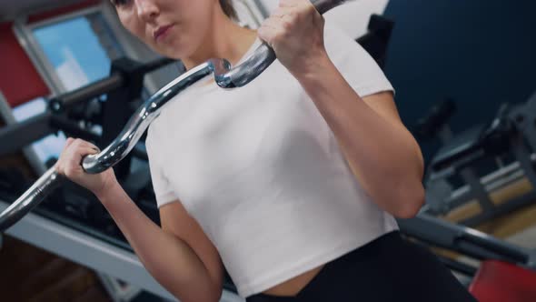 Closeup of a Woman in the Gym Doing an Exercise with Weights to Pump Up the Muscles of Her Arms alt