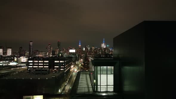 An aerial view over Long Island City, New York at night. A new, empty loft is in the foreground, the alt
