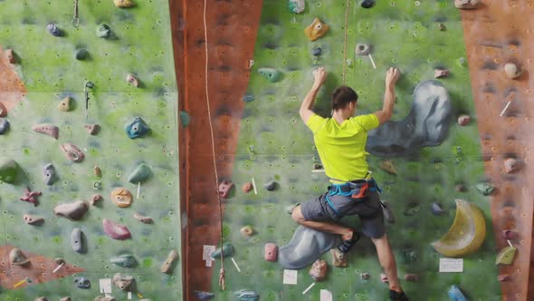 Male Climber Climbs the Cliff Wall in the Room Reaching and Gripping Hold alt