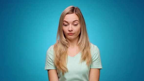 Beautiful Young Woman Grimaces As If Looking at Something Unpleasant Against Blue Background alt