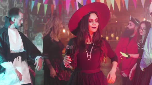 Attractive Woman Disguised As a Witch Dances with a Glass of Blood at a Halloween Party alt