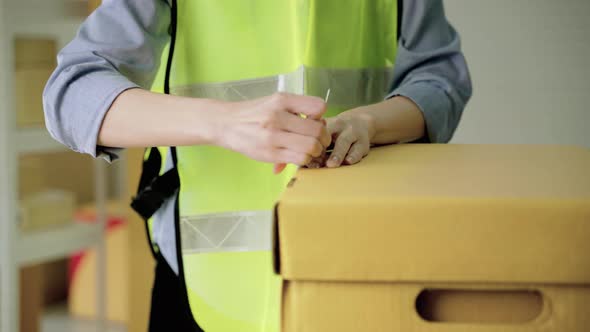 Asian female worker is using straps to finish packing boxes