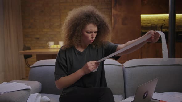 Young 20s Woman Checking Large Expenses Bill and Has Wow Emotion Sitting on Couch at Home alt