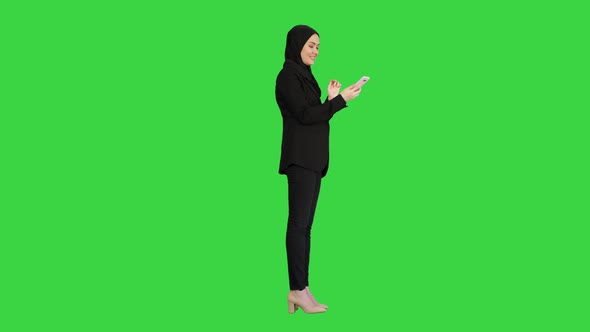 Muslim Girl in Hijab Using Smartphone To Send Voice Messages on a Green Screen, Chroma Key. alt