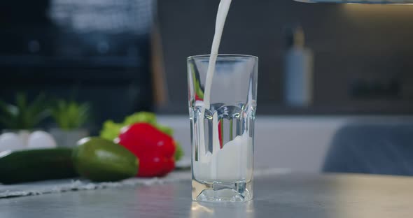 Transparent Glass Standing on Kitchen Table and is Poured with Fresh Milk alt