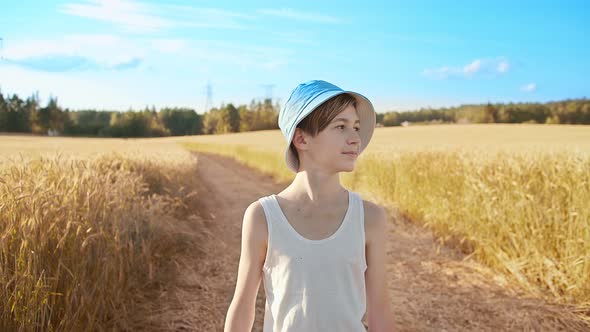 Boy in a Blue Hat Walking Along the Road in the Wheat Field Sunny Weather