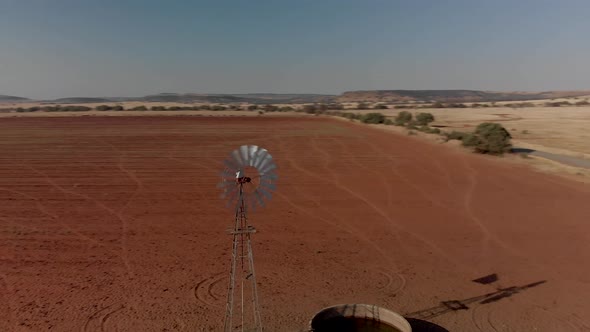 Aerial close up Rotating shot of a working windpump in a dry field alt