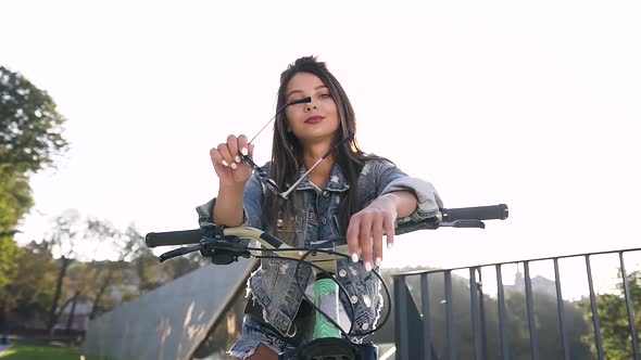 Cheerful Sexy Woman with Long Brown Hair Sitting on Bike and Looking at Camera alt