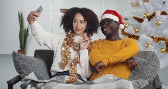 Young Mixed Race Couple Sitting on Sofa in Living Room at Home Celebrating New Year Taking Making alt