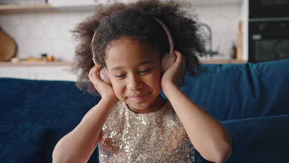 Close Up of Adorable Little African American Girl Listening to Music in Wireless Headphones Dancing alt