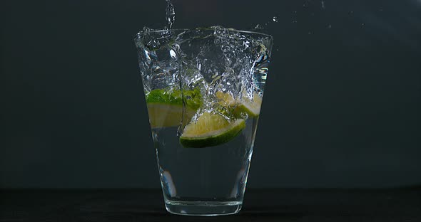 Green Citrus, citrus aurantifolia, falling into a Glass of Water, Slow Motion 4K alt