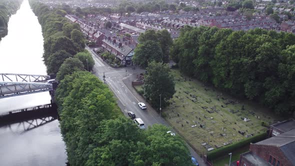 Scenic aerial view above quaint countryside village church cemetery and canal waterway dolly left sh alt