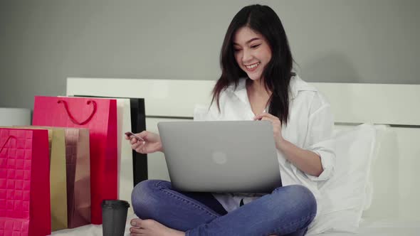 happy woman using laptop computer for online shopping with credit card on a bed