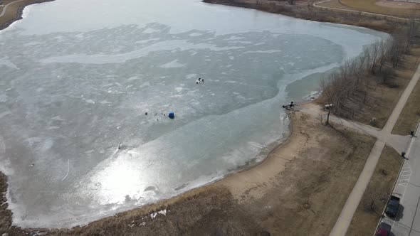 Aerial view of frozen lake with ice fishing happening. Sun gleaming off the ice on lake.