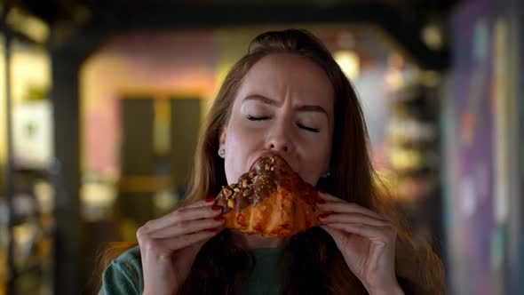 Young Beautiful Girl Greedily Bites a Delicious Fresh Croissant with Chocolate Icing