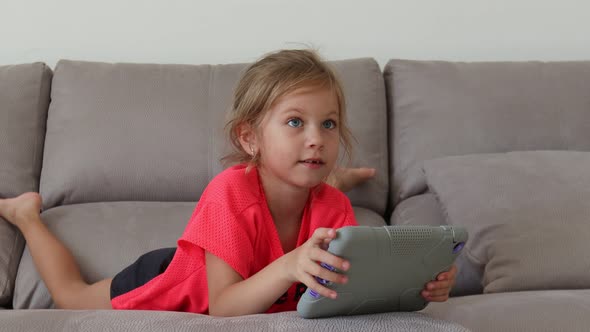 Beautiful Teenager Girl with Tablet Lies on a Sofa in an Apartment