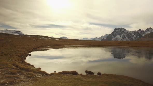 Side POV Walking on Fall Valley Lake and Snowy Mounts Approaching Sunset alt