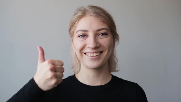 Happy young woman smiling and showing thumb up sign, looking at camera