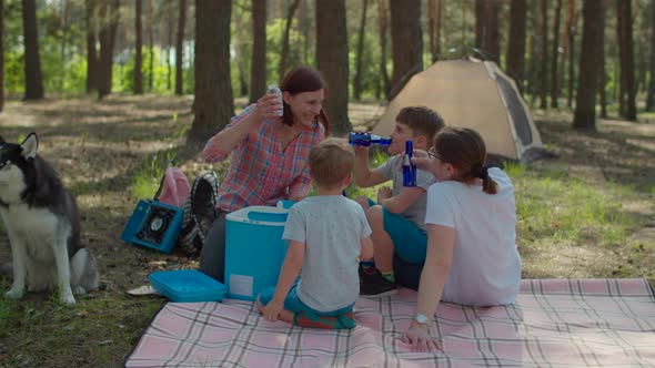 Two moms and two sons drinking cold beverages from fridge on picnic blanket alt