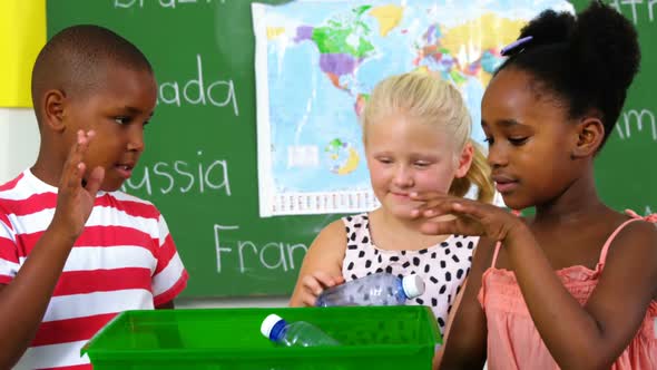 School kids putting waste bottle on recycle logo box in classroom alt