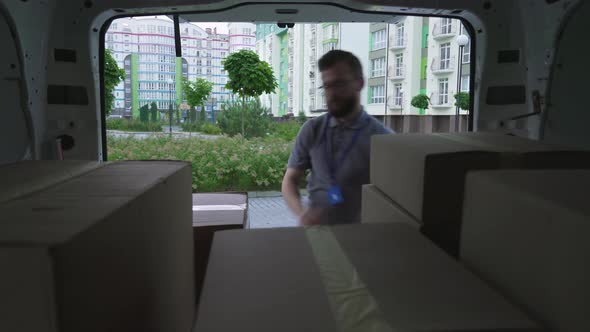 Bearded Courier Putting Paper Boxes Into Opened Van Trunk alt