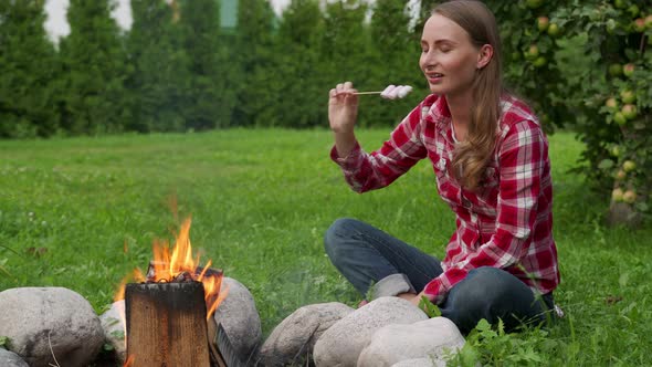Woman Eats Marshmallows While Camping By the Campfire alt