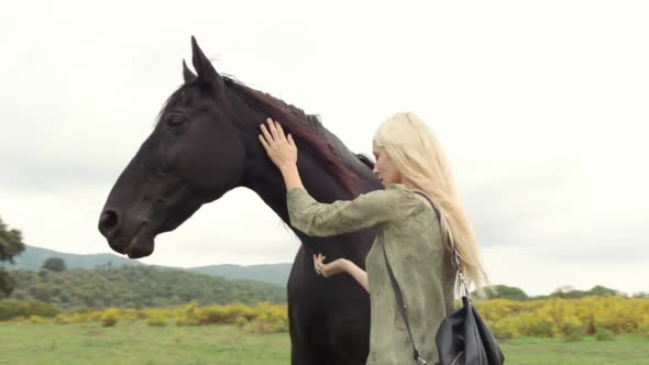 Blonde Young Woman Smiles Strokes and Hugs Black Horse Outdoor and Look at Camera Gimbal Steadicam