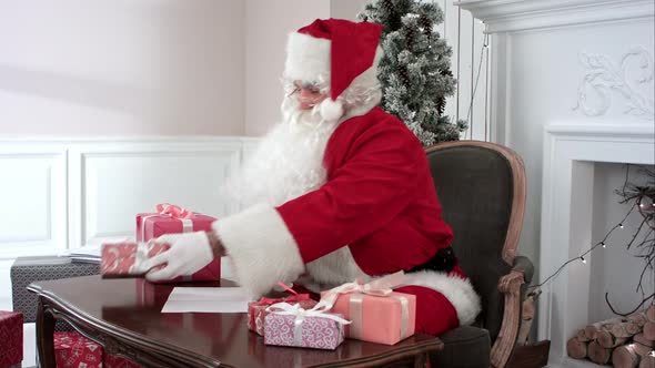 Santa Claus Preparing Presents for Children and Checking the Gift List alt