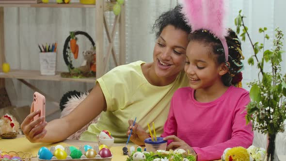 Mom and Daughter with Funny Bunny Ears Talk on a Video Call Using the Phone alt