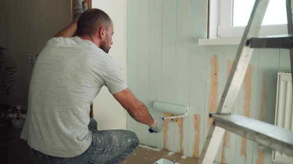 A Man Paints a Wall with a Roller